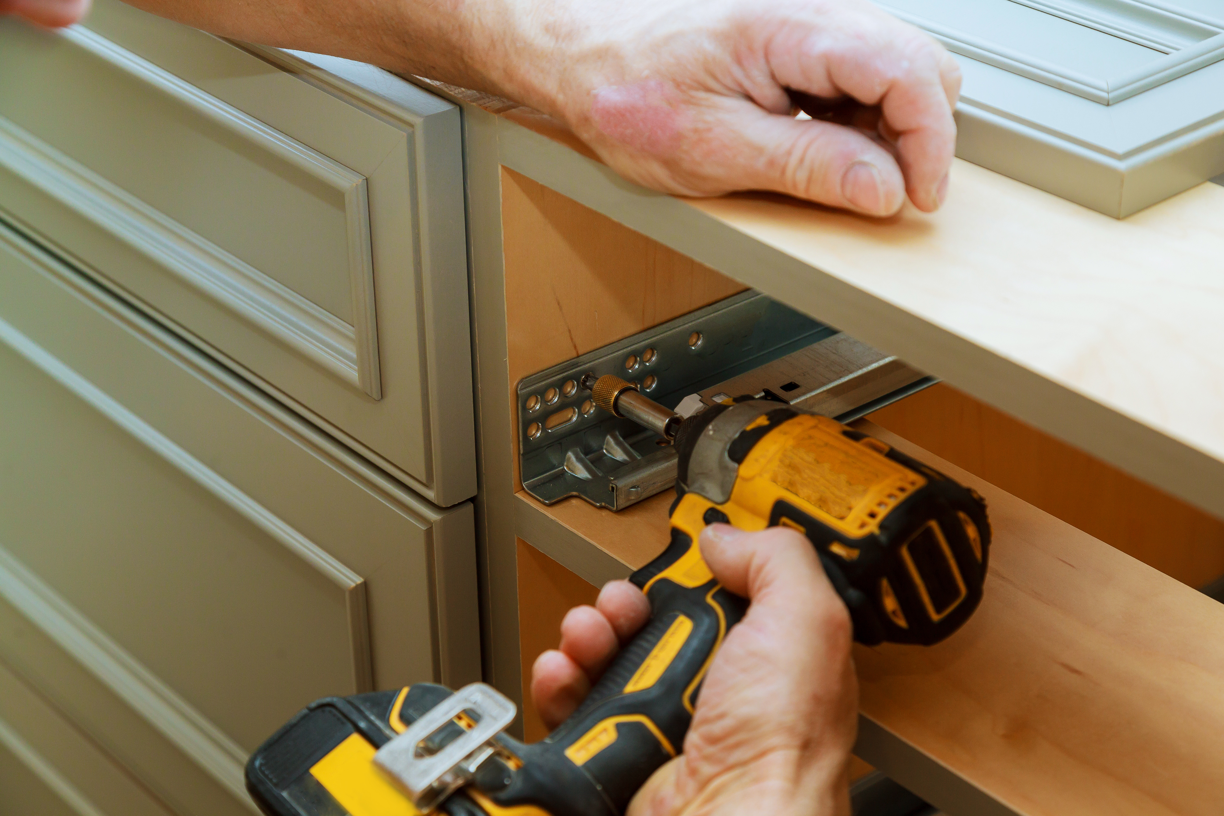 Technician installing dishwasher with power drill under kitchen cabinet