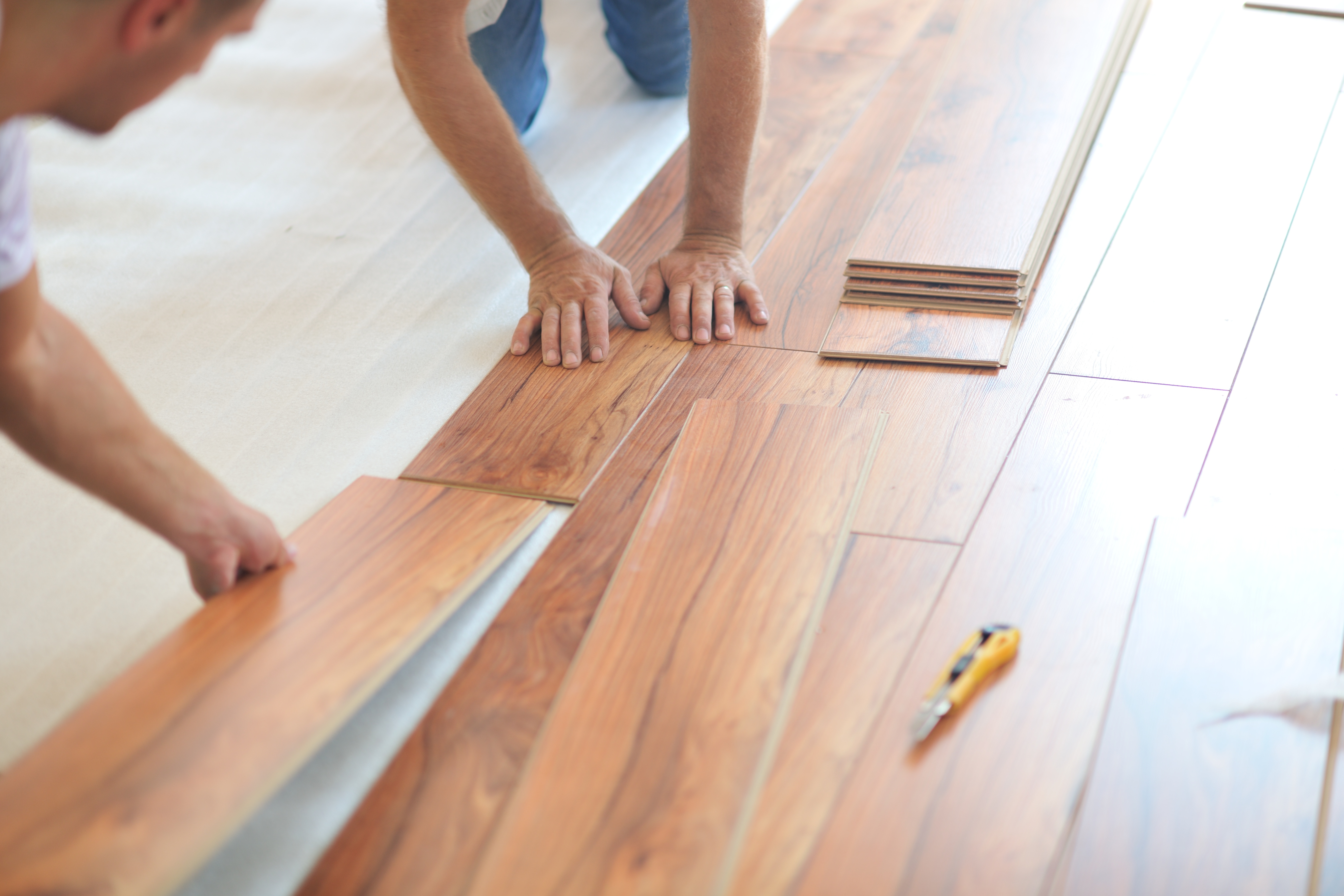 Workers installing laminate wood flooring planks on a subfloor