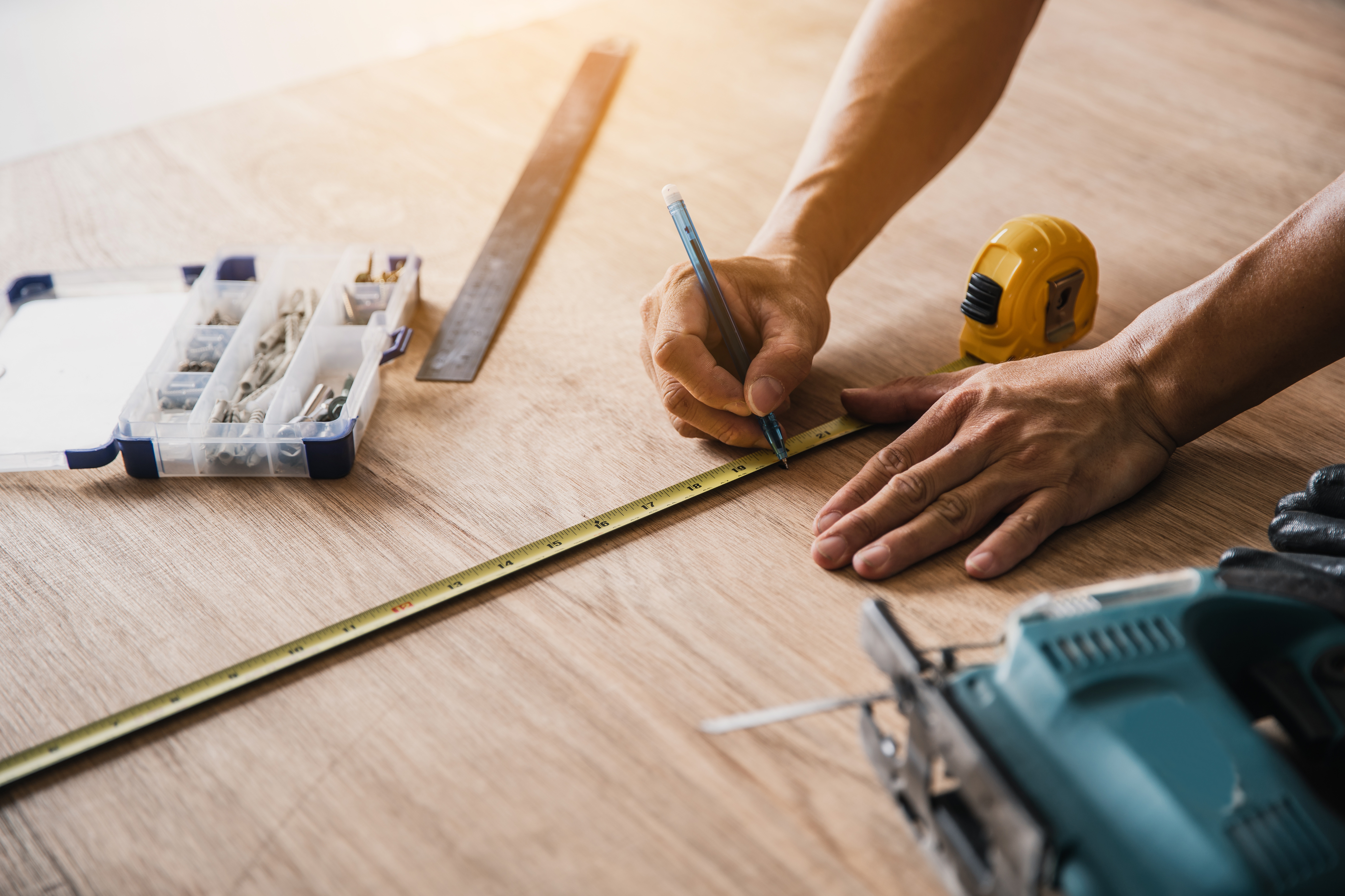 Contractor measuring wooden flooring with tape measure and pencil on light wood surface